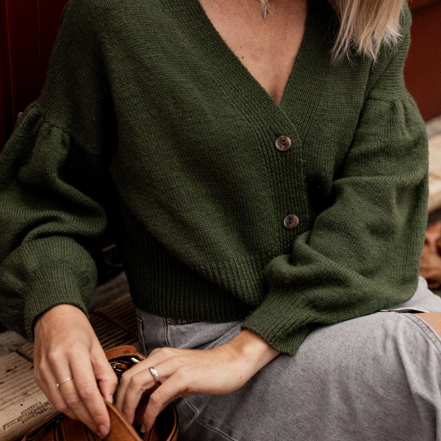 Person wearing a green knitted cardigan and a grey denim skirt sitting on a bench