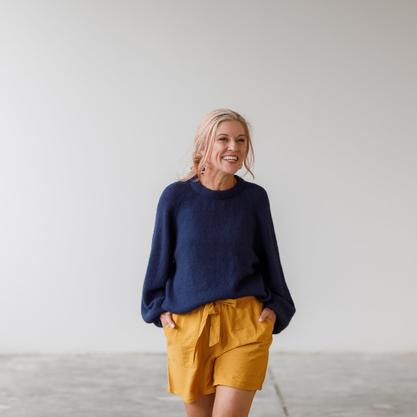 Woman wearing a navy sweater and mustard shorts against a plain background