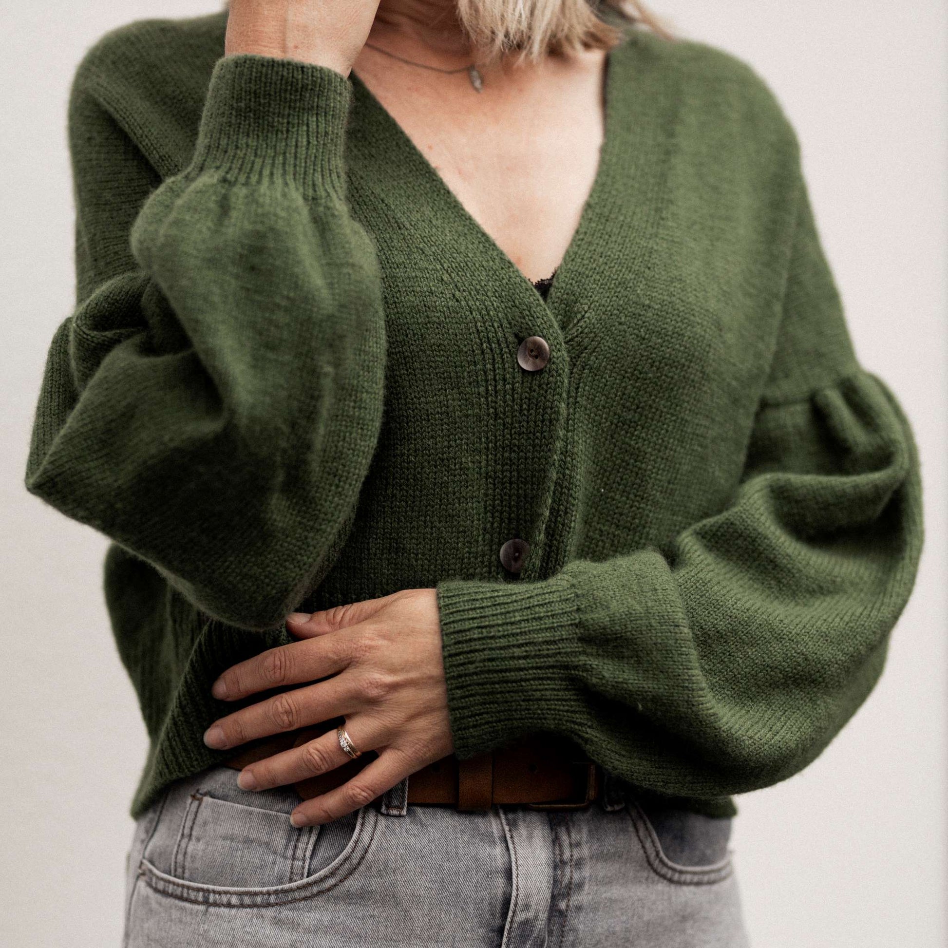Person wearing a green cardigan with puffed sleeves on a plain background